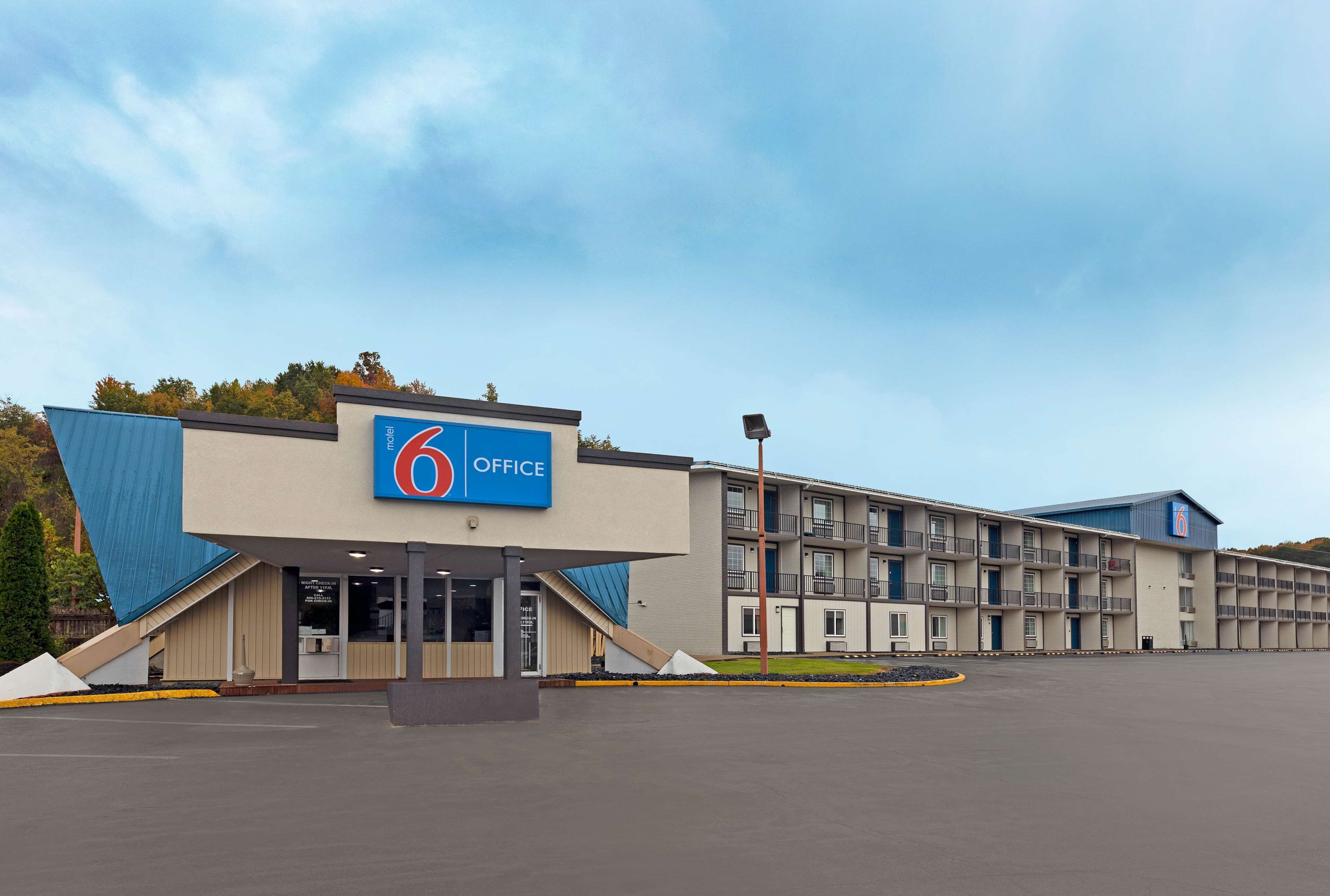 Ein Bürohotel der Kategorie 6 mit modernem Design, erkennbar an einer auffälligen blauen Beschilderung, einem großen Parkplatz und einem mehrstöckigen Gebäude mit Balkonen.