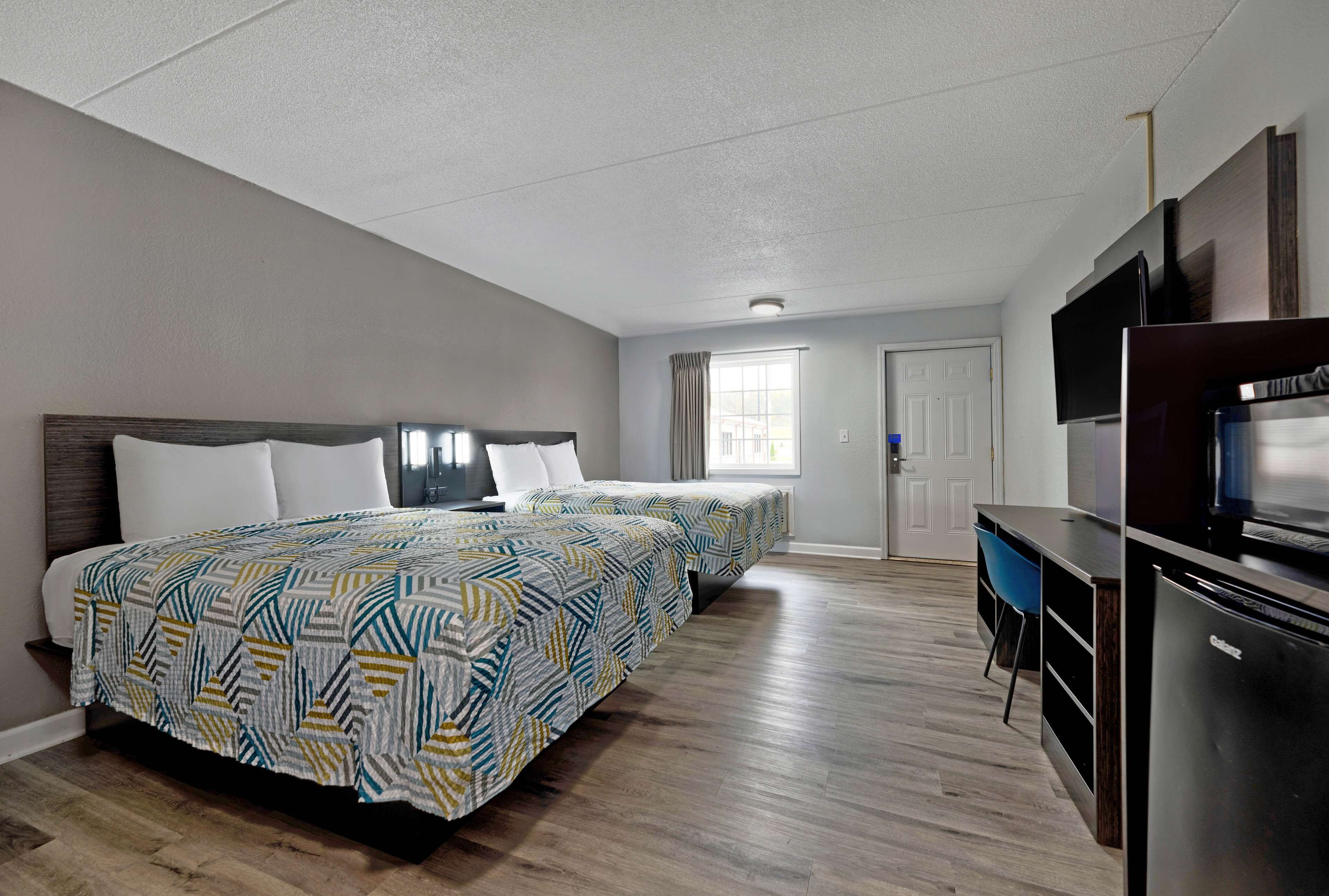 A hotel room with two beds, a desk, a television, and a refrigerator.