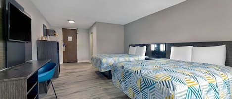 A hotel room with two beds, a desk, a chair, and a TV.
