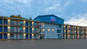 Un motel à étages, avec un grand panneau indiquant le chiffre « 6 », et un parking.