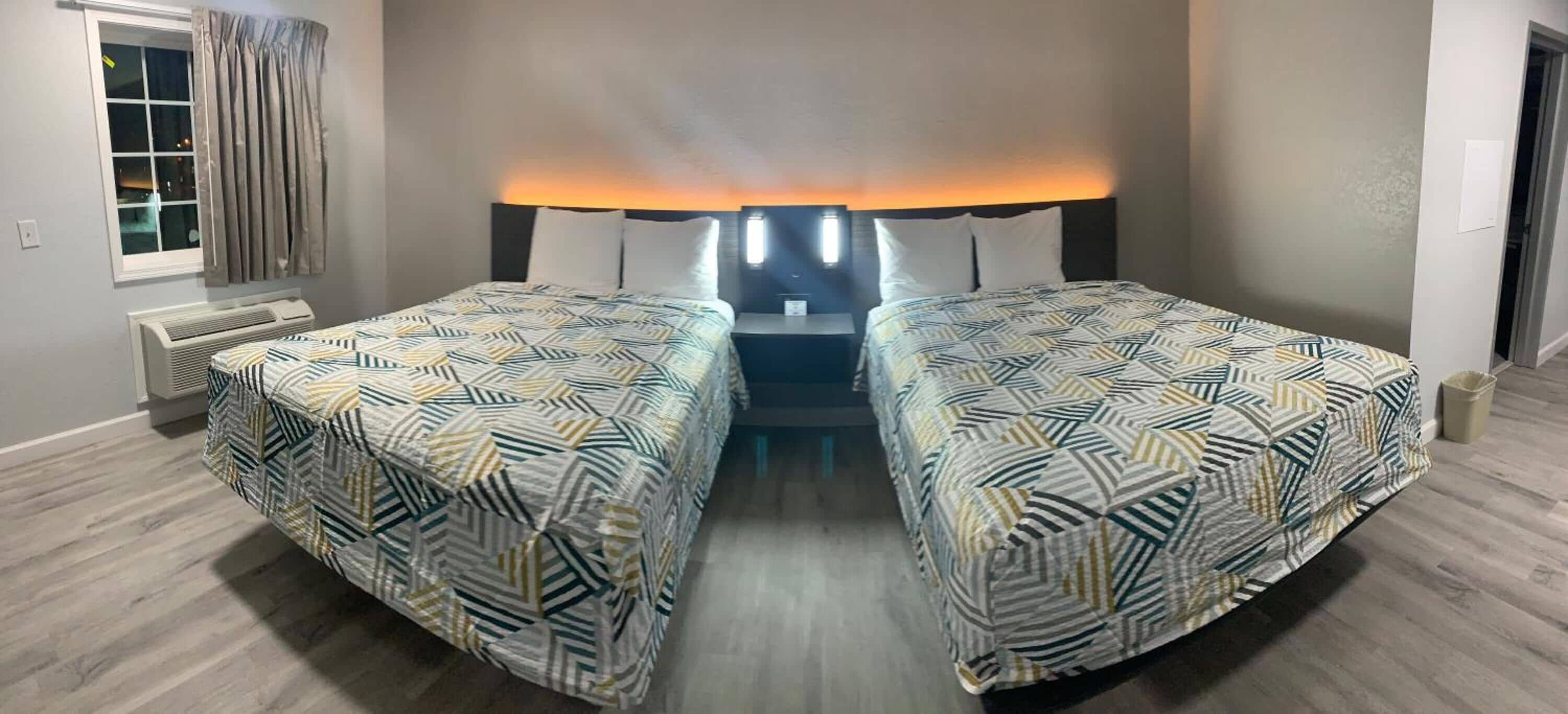 Camera d'albergo con due letti, un comodino, una lampada, una finestra con tende e un termosifone.