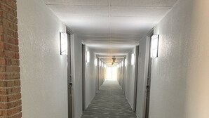 Un long couloir étroit, doté d’un tapis à motifs, de murs blancs et d’un pilier en briques sur le côté gauche.