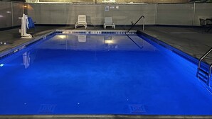 Une piscine rectangulaire à l’eau légèrement bleutée, entourée d’une terrasse carrelée et d’une clôture en métal.