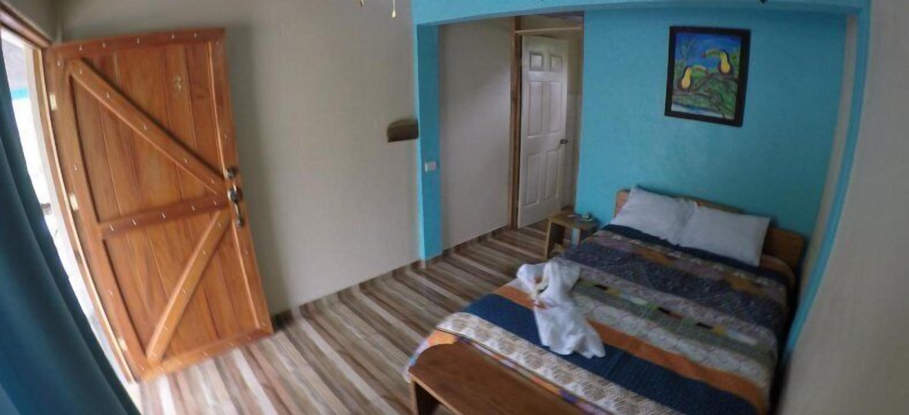 A bedroom with a wooden door, a bed with a colorful quilt, and a painting on the wall.