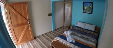 A bedroom with a wooden door, a bed with a colorful quilt, and a painting on the wall.