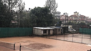 Una cancha de tenis con una red, rodeada por una valla y árboles.