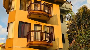 Un edificio de varios pisos con balcones, ventanas amplias y un jardín con plantas en macetas.