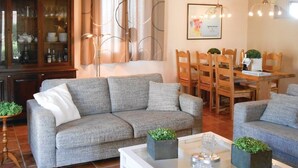 Un salon avec un canapé gris, des chaises en bois, une table à manger et une table basse blanche agrémentée d’objets décoratifs.