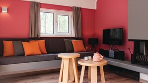 A modern living room with a red wall, a grey sofa with orange cushions, a wooden coffee table, a television, and a fireplace. - Awesome home in Ommen with sauna (Ommen)