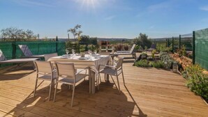 Une terrasse en bois avec une table dressée pour le repas, entourée de chaises, et une vue sur le paysage.