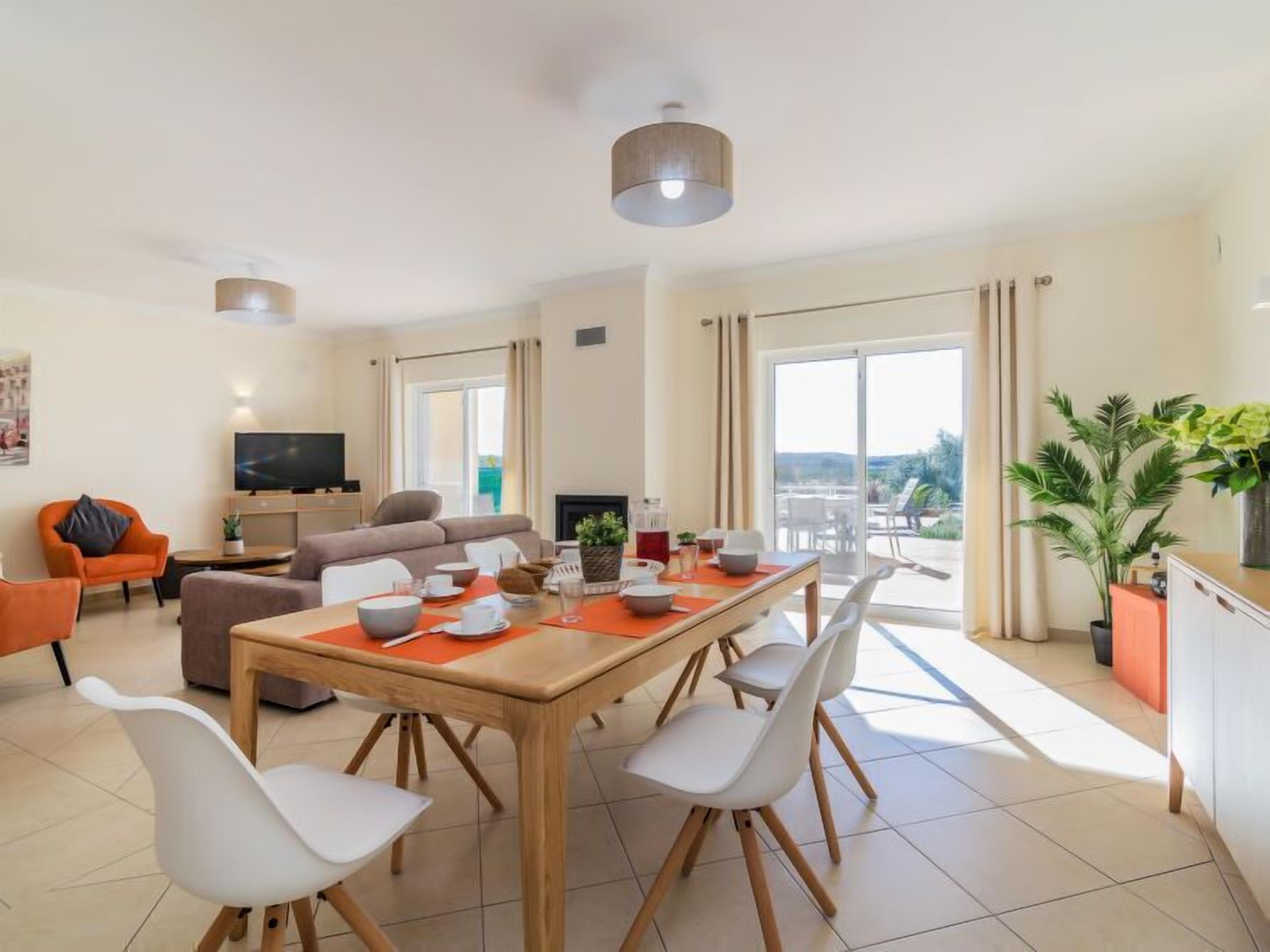 A modern living room with a dining area, a flat-screen TV, and a balcony with a view.