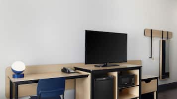Habitación de hotel moderna con escritorio de madera, televisor de pantalla plana, refrigerador pequeño y una silla azul.