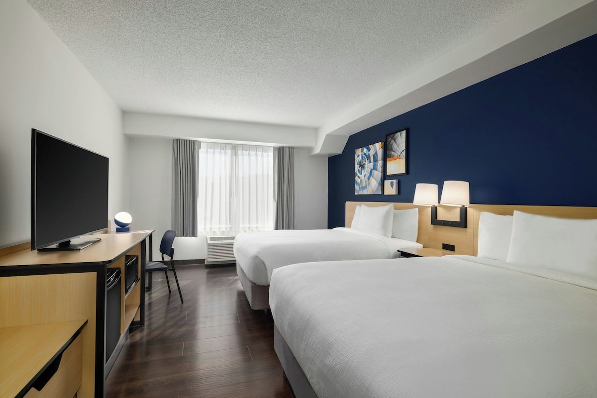A hotel room with two beds, a desk with a TV, a chair, and a window with curtains.