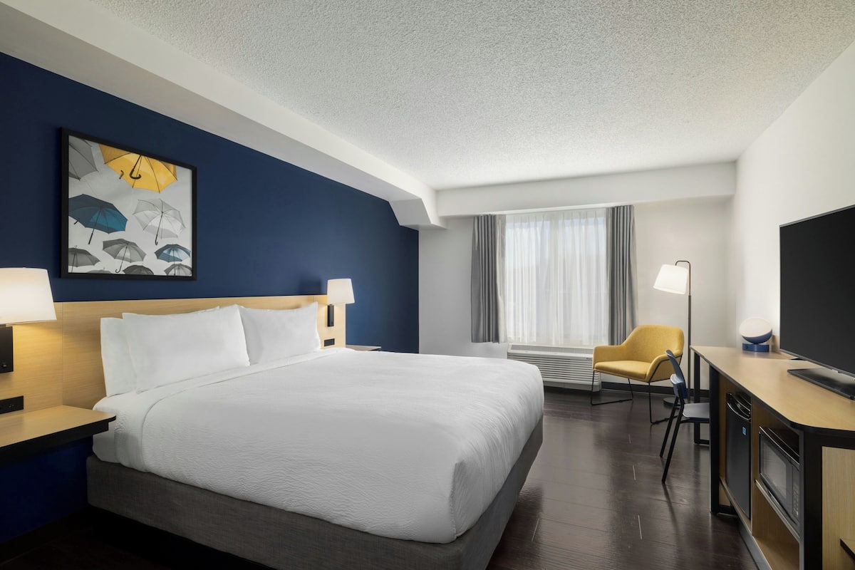 A hotel room with a large bed, a desk with a flat-screen TV, a chair, and a wall-mounted artwork.