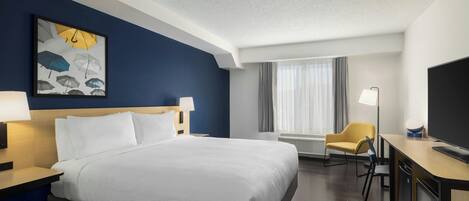 Une chambre d’hôtel avec un grand lit, un bureau doté d’un téléviseur à écran plat, une chaise et une œuvre d’art accrochée au mur.