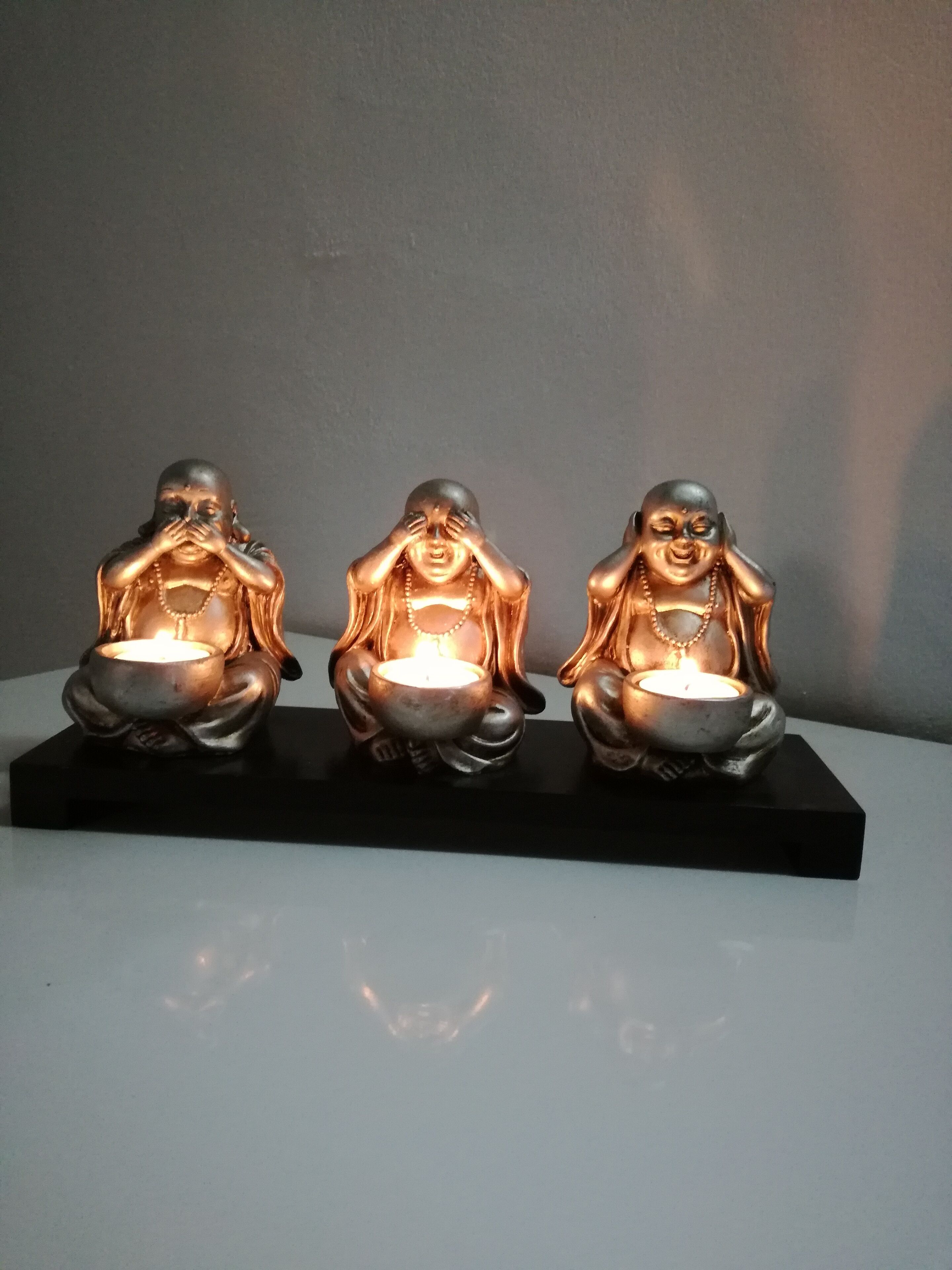 Three bronze statues of seated figures with candles, placed on a black base.