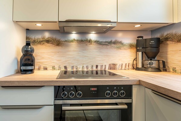 A modern kitchen with a built-in stove, a coffee maker, and a JUNKER brand extractor hood.