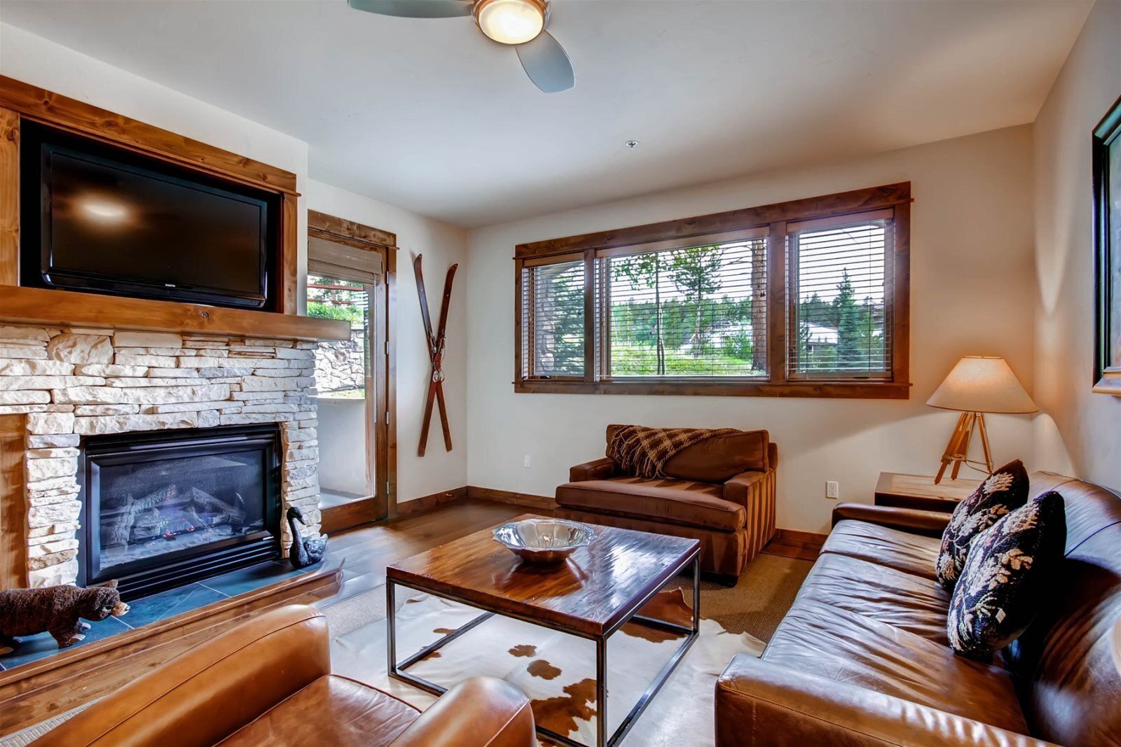 A living room with a stone fireplace, leather sofas, a coffee table, and a television mounted above the fireplace.