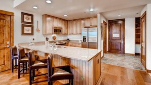 A spacious kitchen with wooden cabinets, a large island with bar stools, stainless steel appliances, and a stone backsplash. - Luxury 3 Bedroom Ski in, Ski Out Mountain Vacation Rental Just Steps from the Snowflake Ski Lift (Breckenridge)