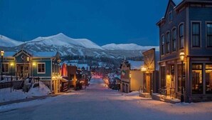 A snow-covered street with buildings and a mountain in the background. - Luxury 3 Bedroom Ski in, Ski Out Mountain Vacation Rental Just Steps from the Snowflake Ski Lift (Breckenridge)