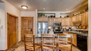 A kitchen with wooden cabinets, a stainless steel refrigerator, a microwave, a stove, and a dishwasher. There are three wooden chairs at the kitchen island. - Premier 2 Bedroom Mountain View Condo Located in Historic Downtown Breckenridge Walking Distance to Peak 9 (Breckenridge)