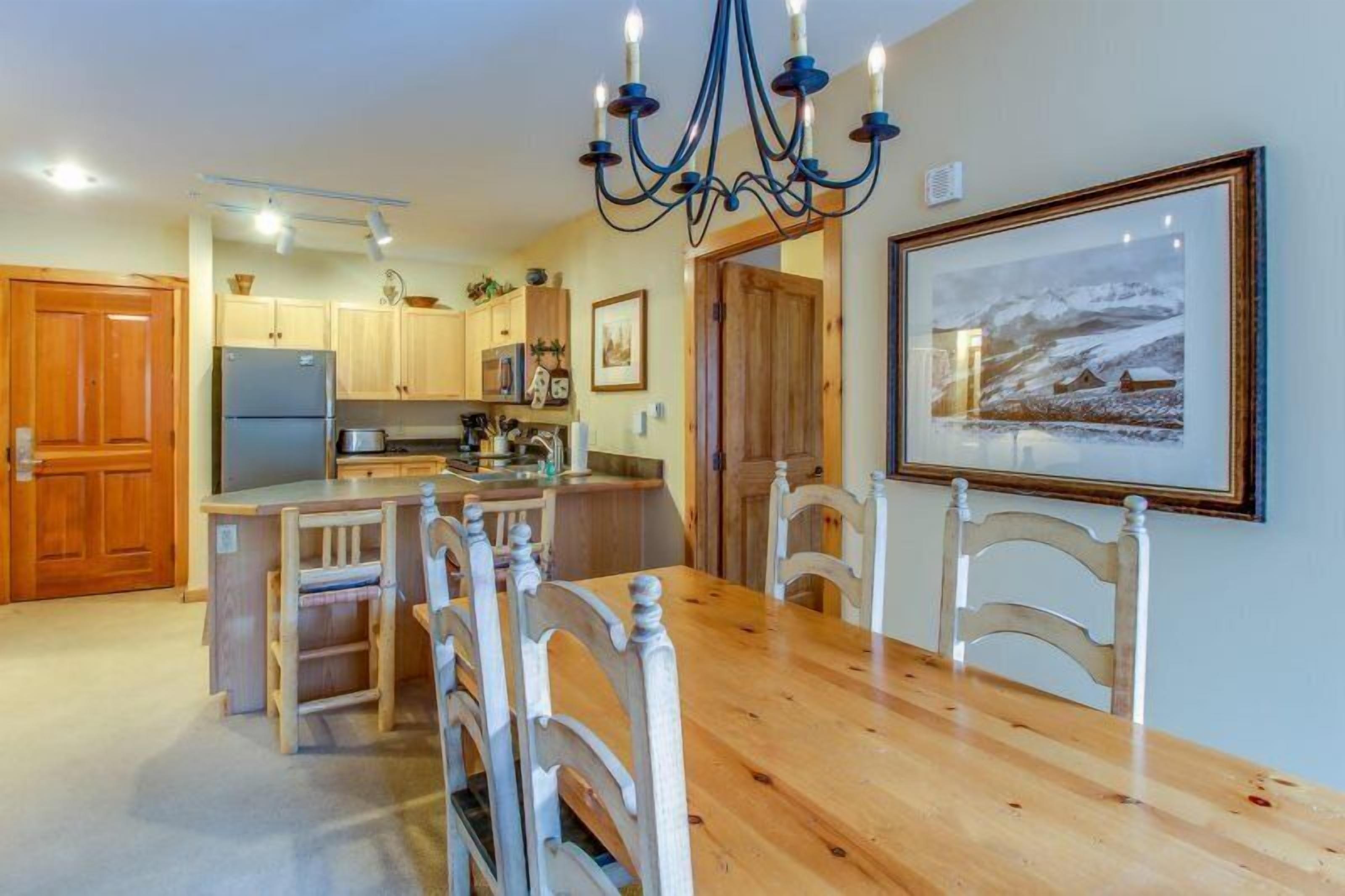 Une cuisine avec des meubles en bois, un réfrigérateur, une table à manger avec des chaises et un lustre.