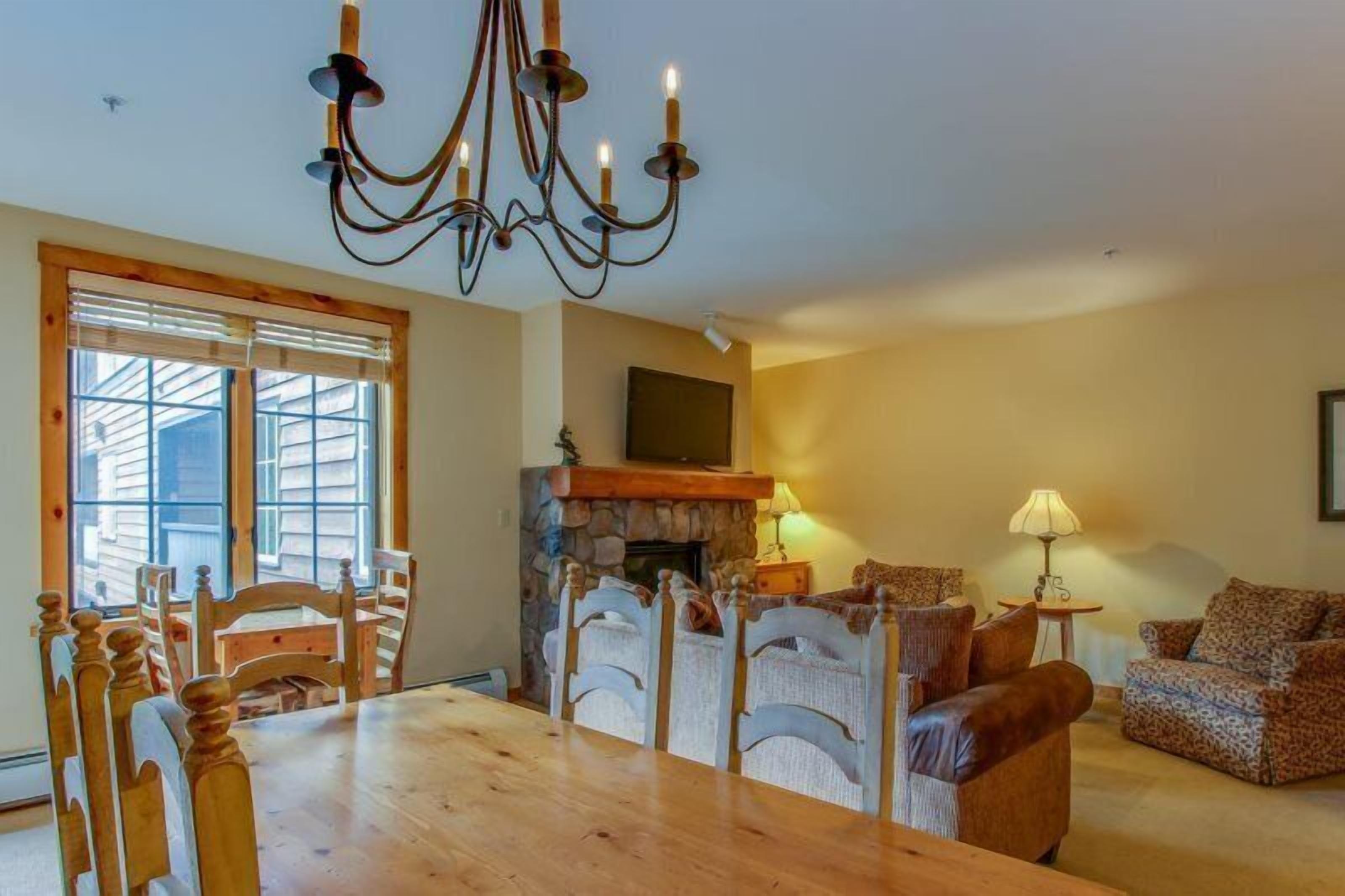 A dining area with a wooden table and chairs, a stone fireplace, and a chandelier.