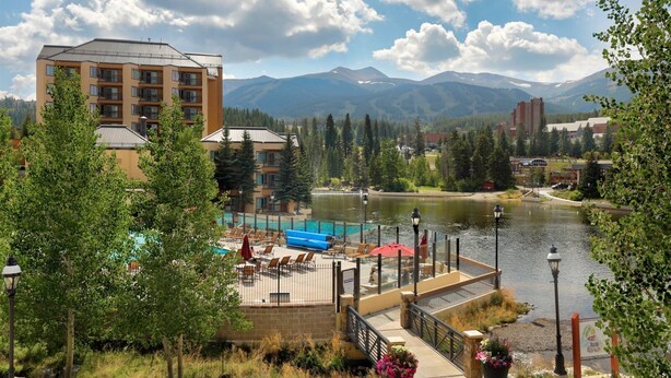 A hotel with a pool area, a bridge, and mountains in the background.