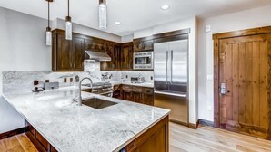 A modern kitchen with a large island, stainless steel appliances, wooden cabinets, and pendant lighting.