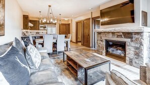 A modern living room with a stone fireplace, a dining area, and a kitchen in the background.