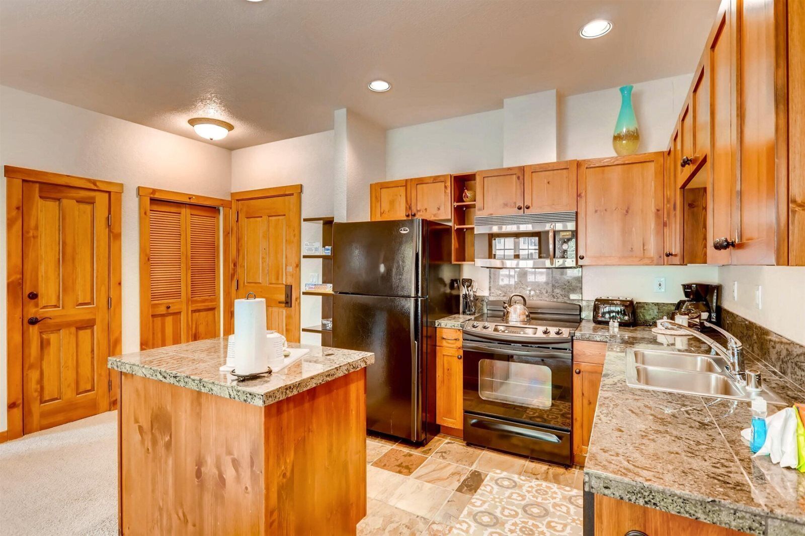 A kitchen with wooden cabinets, a black refrigerator, a stove, and granite countertops.