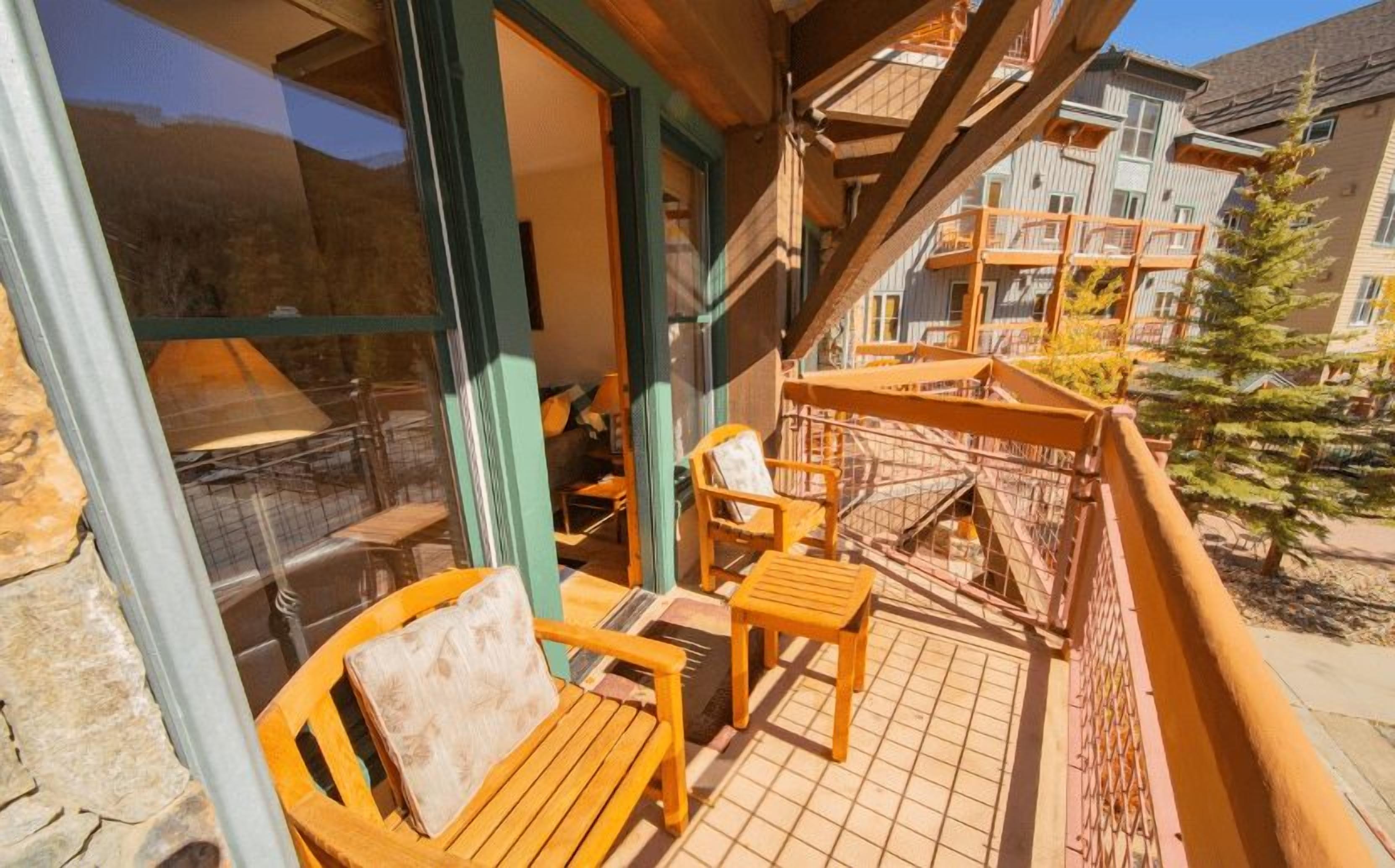 A balcony with wooden furniture, a glass door leading to a room, and a view of a residential area.