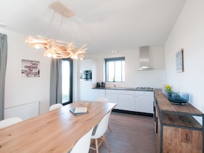 Une cuisine moderne avec des meubles blancs, une table à manger en bois et un luminaire suspendu.