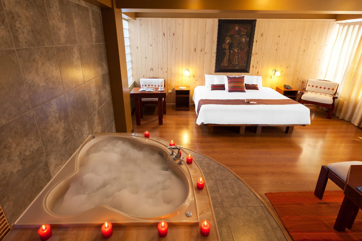 Ein Hotelzimmer mit Herzförmigem Whirlpool, einem großen Bett, zwei Nachttischen, einem Sessel und einem Bild an der Wand.