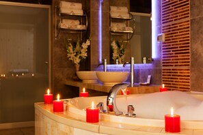 A bathroom with a large bathtub, multiple red candles, a sink, and a mirror. - Chaski Hotel (Cusco)