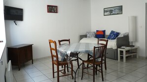 A small, well-lit room with a dining table, chairs, a bed with pillows, a TV, and a bedside table. - apartment of the callade (Peyriac-de-Mer)
