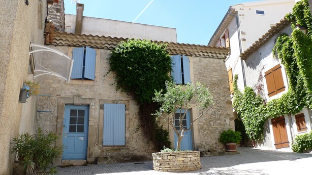 A narrow cobblestone street with stone buildings, blue shutters, and potted plants. - apartment of the callade (Peyriac-de-Mer)