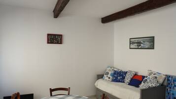 Una habitación con una cama, una mesa y una silla. Hay un cuadro en la pared y una pequeña mesa con mantel a cuadros.