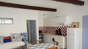 A compact kitchen with a washing machine, a microwave, and a coffee maker. There is a dining table with chairs and a bed with patterned pillows. - apartment of the callade (Peyriac-de-Mer)
