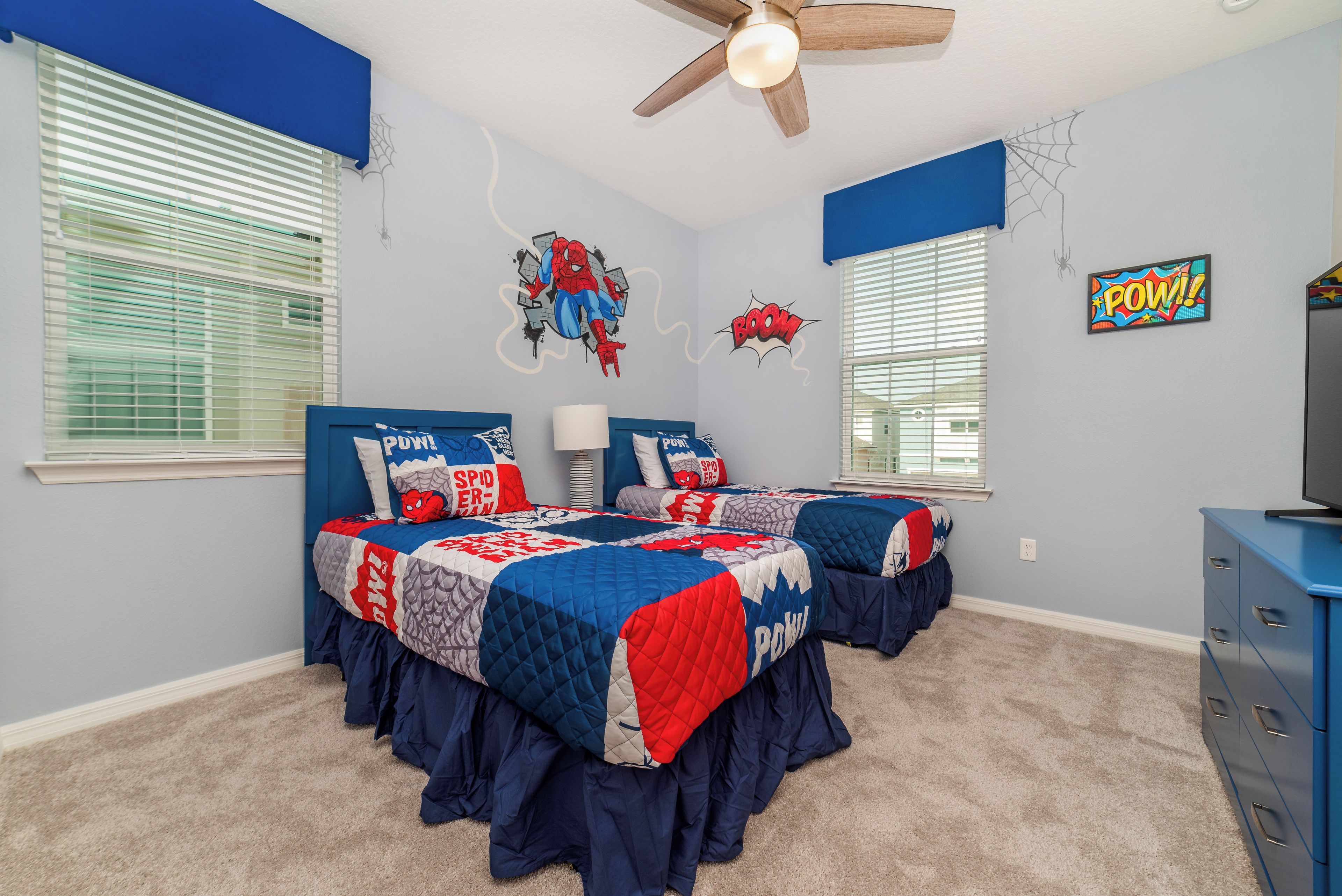 Une chambre avec deux lits, un ventilateur de plafond et des décorations sur le thème de Spider-Man.