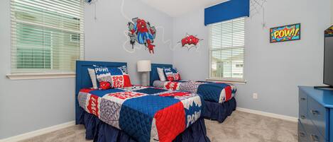 Une chambre avec deux lits, un ventilateur de plafond et des décorations sur le thème de Spider-Man.