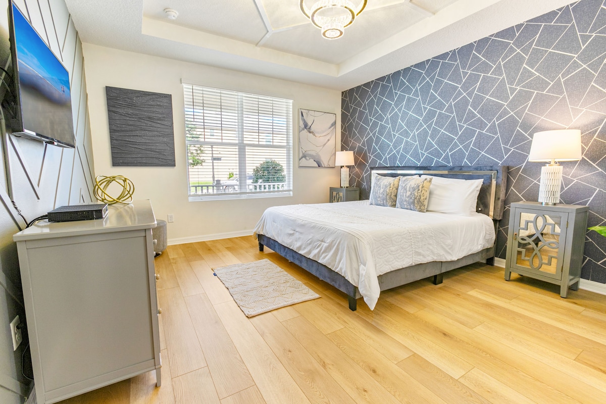 A bedroom with a bed, bedside tables, a TV, a window, and a patterned wall.