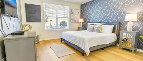 A bedroom with a bed, bedside tables, a TV, a window, and a patterned wall.