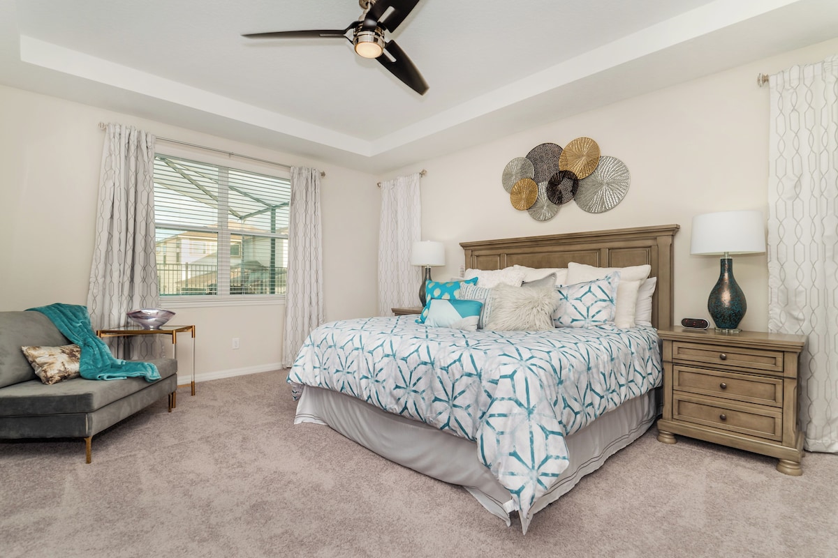 A bedroom with a bed, bedside tables, a nightstand, a ceiling fan, and a window with curtains.