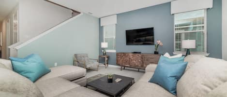 A living room with a sofa set, a coffee table, a TV, and a staircase.