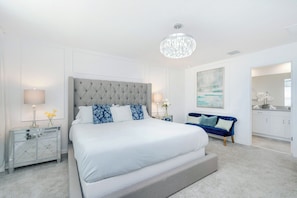 A bedroom with a large bed, two bedside tables, a chandelier, a blue sofa, and a painting on the wall.
