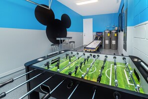 A foosball table in a room with blue walls, a Mickey Mouse mural, and two water coolers. - Solara Resort Homes and Townhomes (Kissimmee)