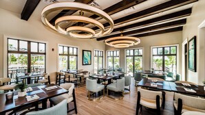 A spacious dining area with multiple tables and chairs, large windows, and a modern ceiling design.