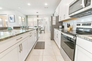 Uma cozinha moderna com armários brancos, bancadas de granito e eletrodomésticos de aço inoxidável, além de uma ilha grande.