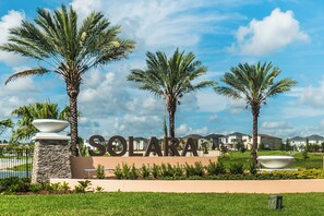 A sign with the name 'SOLARA' surrounded by palm trees and a well-maintained lawn. - Solara Resort Homes and Townhomes (Kissimmee)